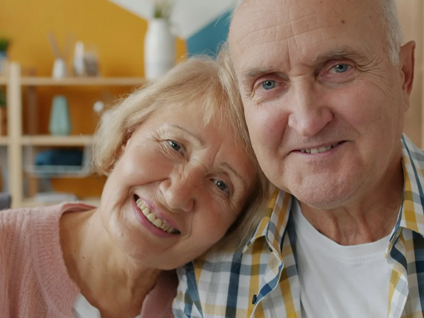 Una pareja de adultos mayores sonríe, abrazada y relajada, en su casa.